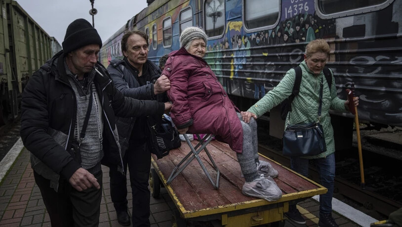 Angehörige einer älteren Frau transportieren sie zu einem Evakuierungszug in Cherson. Foto: Evgeniy Maloletka/AP/dpa