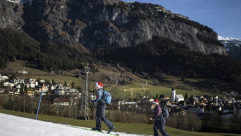 Zwei Skitourengänger mit Weihnachtsmann-Mützen am 25. Dezember auf einem Kunstschneeflecken in Flims GR.