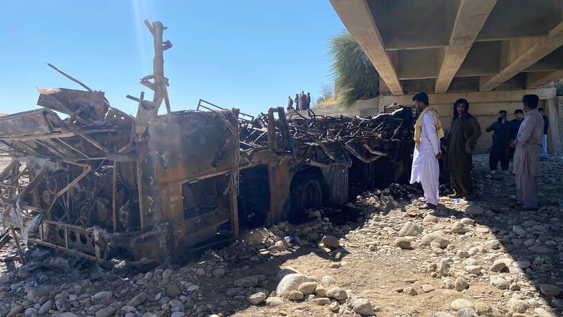 Menschen betrachten das verbrannte Wrack eines verunglückten Busses, der mit rund 50 Menschen an Bord in eine Schlucht gestürzt ist. Foto: Muhammad Saleem/AP/dpa