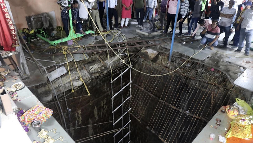 Menschen neben einem alten Brunnenbauwerk, über das ein Tempelboden gebaut wurde, der eingebrochen ist. In Indien sind mehrere Menschen gestorben und weitere verletzt worden, nachdem der Boden in einem Tempel eingebrochen wa Foto: AP/dpa