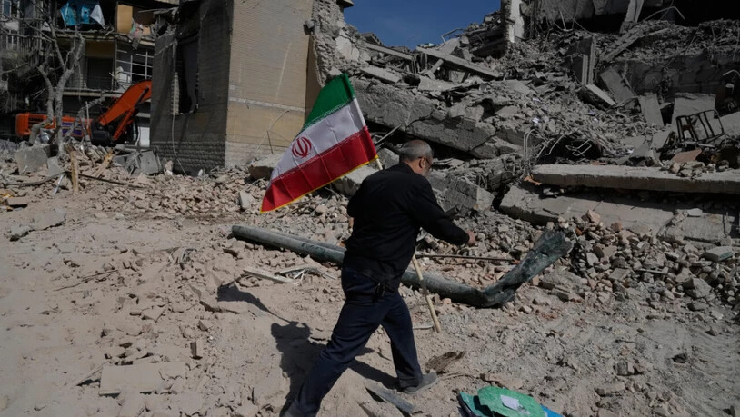 Ein Mann trägt eine iranische Flagge und legt sie auf die Trümmer einer Polizeieinrichtung, die während der amerikanisch-israelischen Militäraktion  getroffen wurde. Foto: Vahid Salemi/AP/dpa