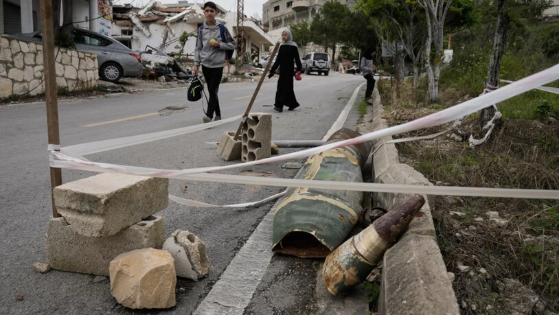 Menschen gehen neben Raketenteilen im Dorf Halloussiyeh im Südlibanon vorbei. Foto: Bilal Hussein/AP/dpa