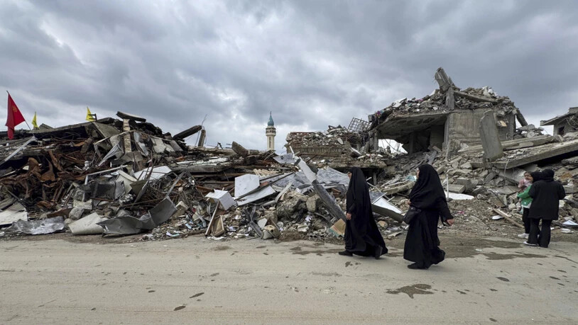 ARCHIV - Einwohner gehen an zerstörten Gebäuden im Libanon vorbei (Archivbild). Foto: Bassam Hatoum/AP/dpa