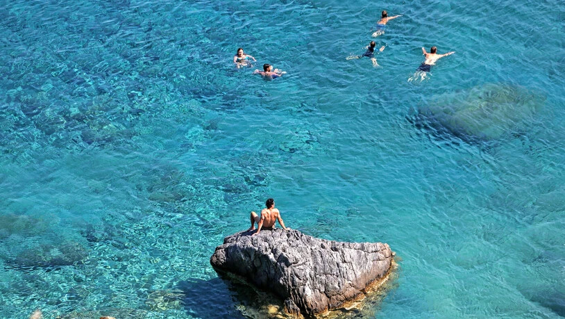 Kristallklares Wasser: Feriengäste schwimmen entlang eines felsigen Strands auf der griechischen Insel Amorgos.