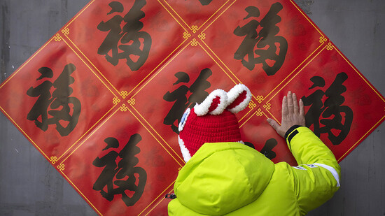 Eine Frau in Peking glättet mit ihrer Hand die Dekoration für das bevorstehende Mondneujahr. Foto: Mark Schiefelbein/AP/dpa