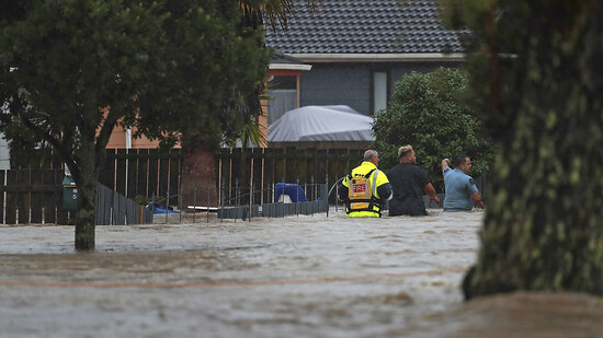 Rettungskräfte und ein Mann waten durch das Hochwasser einer überschwemmter Straße. Foto: Hayden Woodward/New Zealand Herald/AP/dpa