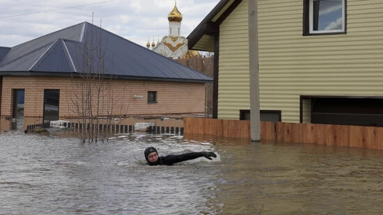 dpatopbilder - Ein Anwohner schwimmt in der überfluteten Straße zwischen Häusern in Orenburg. Foto: Uncredited/AP