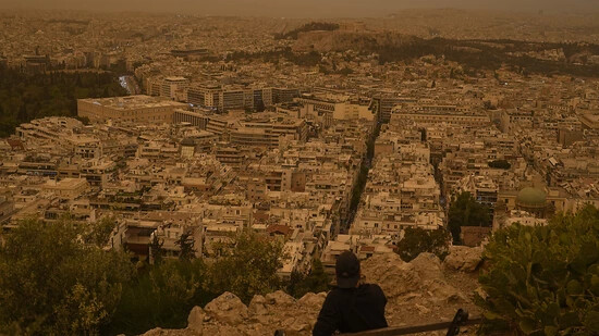 dpatopbilder - Ein Tourist sitzt auf einer Bank auf dem Lycabettus-Hügel in Athen. Saharastaub hat den Himmel über der griechischen Hauptstadt eingetrübt. Foto: Petros Giannakouris/AP/dpa