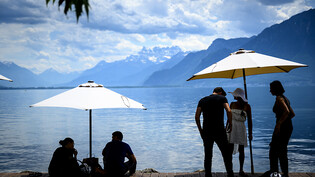Menschen geniessen am Genfersee unter Sonnenschirmen das unverhofft frühe Sommerwetter.