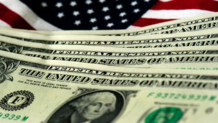 ARCHIV - US-amerikanische Geldscheine sind vor einer USA-Fahne zu sehen. Foto: Arno Burgi/dpa-Zentralbild/dpa