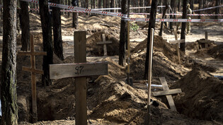 Ein Holzkreuz markiert ein nicht identifiziertes Grab während einer Exhumierung auf dem Waldfriedhof von Isjum. Foto: Evgeniy Maloletka/AP/dpa