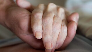 Ein Altenpfleger hält in einem Pflegeheim die Hand einer Frau. (Symbolbild)