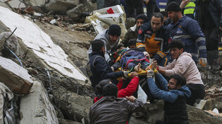 Menschen und Rettungskräfte bergen eine Person auf einer Bahre aus einem eingestürzten Gebäude. Foto: Elifaysenurbay/IHA/AP/dpa