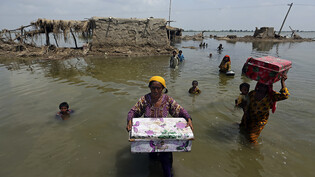 ARCHIV - Frauen tragen Habseligkeiten aus ihrem durch heftige Regenfälle im Jahr 2022 überschwemmten Haus in der pakistanischen Provinz Sindh. Die pakistanische Hauptstadt Islamabad ist heute von einem heftigen Erdbeben erschüttert worden. Foto: Fareed…