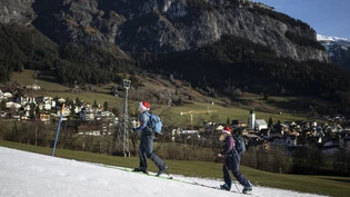 Weiss auf Grün: Zwei Skitourengänger laufen am Weihnachtstag auf einem Band Kunstschnee von Flims Richtung Berg. 